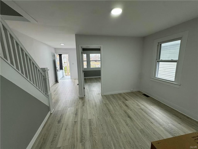 unfurnished room featuring baseboards, light wood-type flooring, visible vents, and stairway