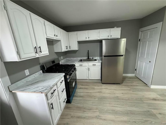 kitchen with light wood finished floors, a sink, white cabinetry, and appliances with stainless steel finishes