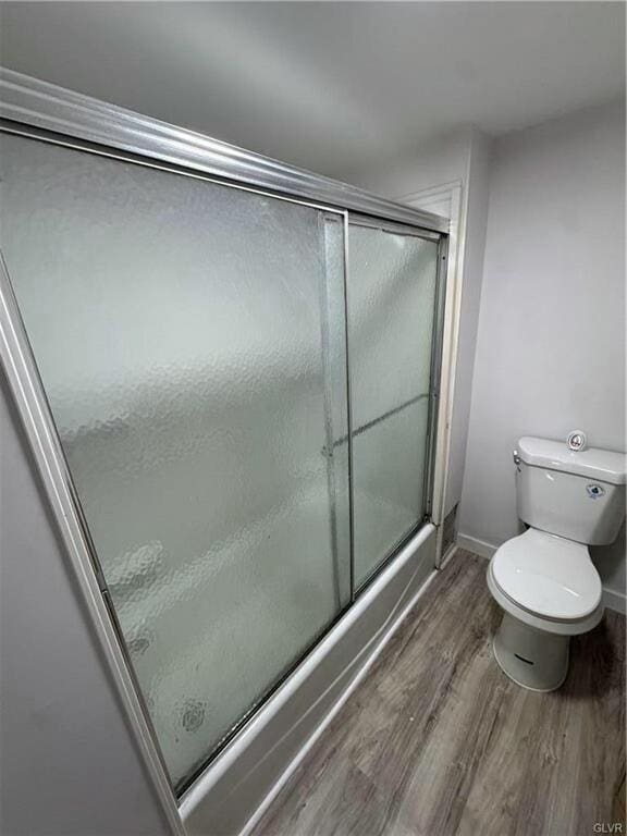 full bathroom featuring a shower with door, baseboards, wood finished floors, and toilet