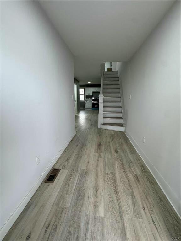 hall featuring baseboards, stairs, visible vents, and wood finished floors