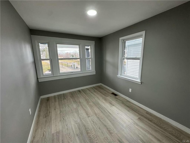 spare room with baseboards, light wood finished floors, and visible vents