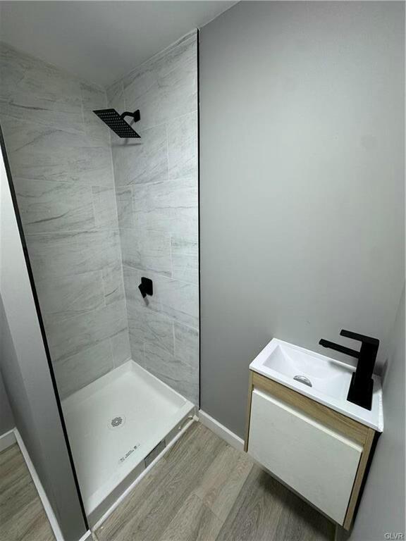 full bathroom featuring vanity, baseboards, wood finished floors, and tiled shower