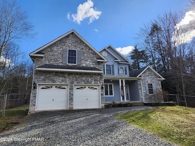 traditional home featuring stone siding, an attached garage, driveway, and fence