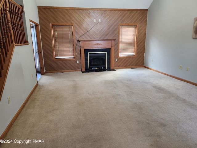 unfurnished living room featuring wooden walls, visible vents, baseboards, a fireplace, and carpet flooring