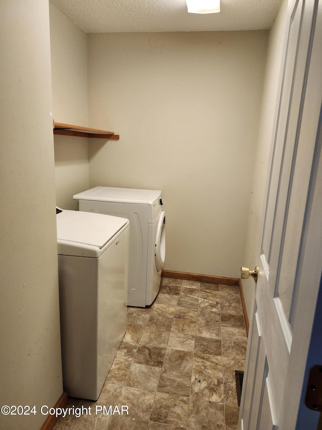 clothes washing area with baseboards, separate washer and dryer, laundry area, and a textured ceiling