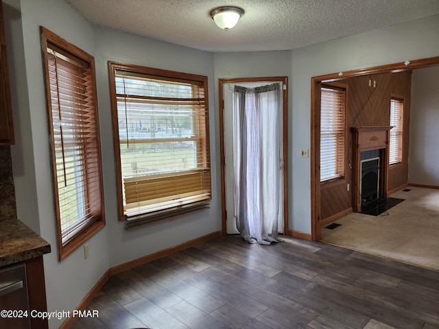 unfurnished living room featuring a healthy amount of sunlight, a textured ceiling, baseboards, and dark wood-style flooring