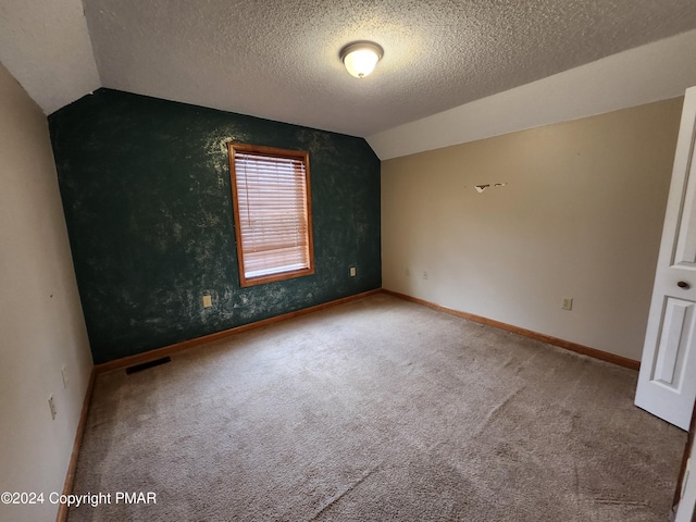 empty room featuring visible vents, baseboards, carpet, lofted ceiling, and a textured ceiling