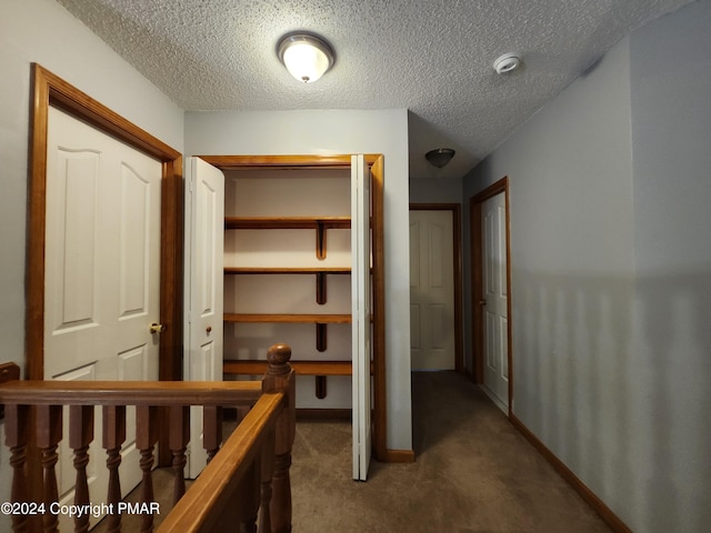 corridor with an upstairs landing, carpet, baseboards, and a textured ceiling