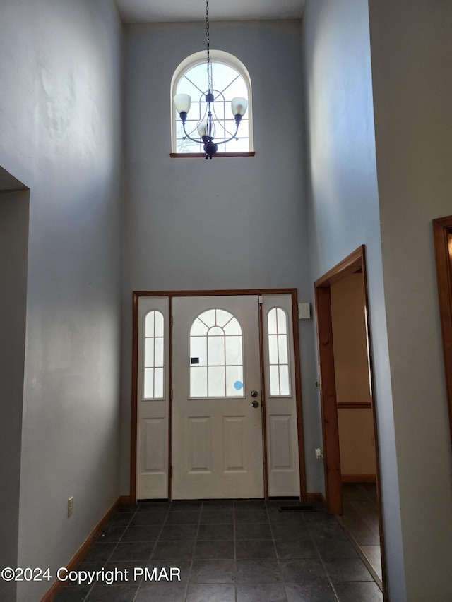 tiled foyer entrance with a notable chandelier, a high ceiling, and baseboards