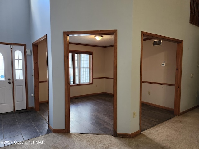 carpeted foyer entrance featuring crown molding, visible vents, and baseboards