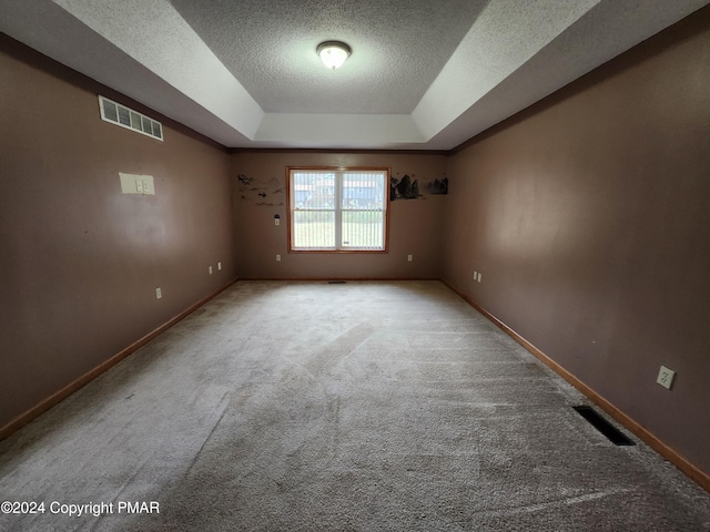 carpeted empty room with visible vents, a textured ceiling, a raised ceiling, and baseboards