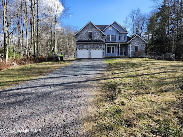 traditional-style house featuring fence, gravel driveway, an attached garage, a front lawn, and stone siding