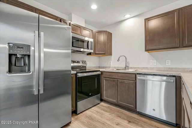 kitchen featuring stainless steel appliances, light countertops, light wood-style floors, a sink, and recessed lighting