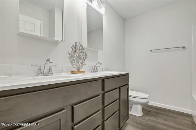 bathroom with toilet, wood finished floors, a sink, baseboards, and double vanity