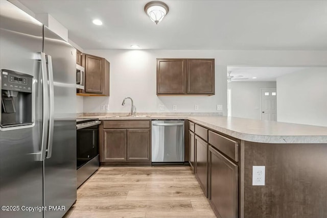 kitchen with light wood-style flooring, a peninsula, a sink, light countertops, and appliances with stainless steel finishes