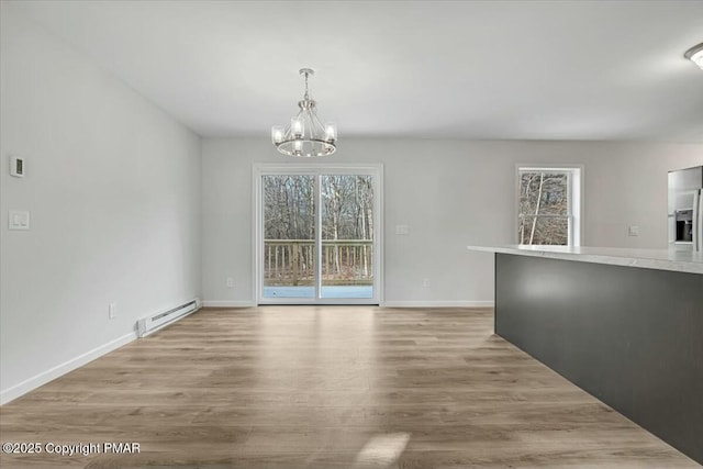 unfurnished dining area featuring light wood-type flooring, plenty of natural light, a baseboard radiator, and a chandelier