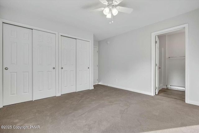 unfurnished bedroom featuring baseboards, a baseboard radiator, ceiling fan, carpet flooring, and two closets