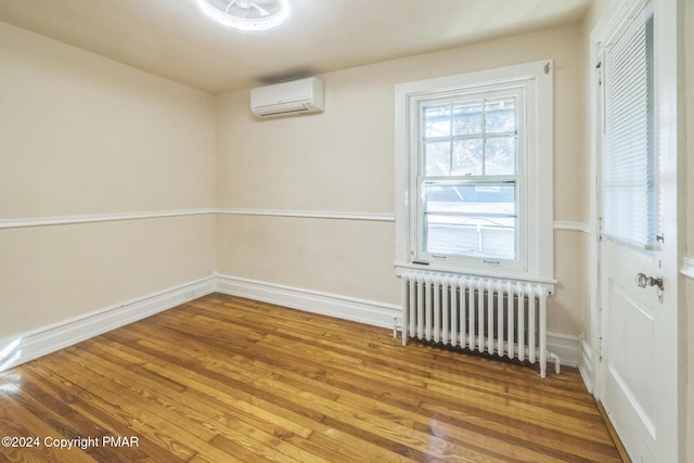 spare room with radiator, baseboards, wood finished floors, and a wall mounted AC