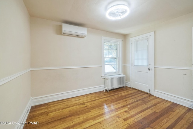 unfurnished room with radiator, a wall unit AC, baseboards, and hardwood / wood-style floors