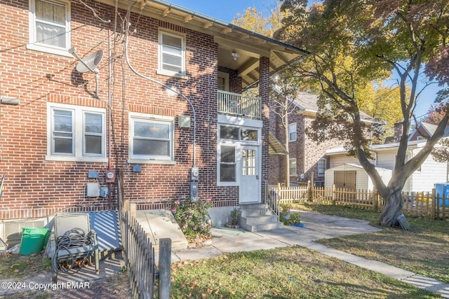 view of front of home with a balcony, entry steps, fence, and brick siding