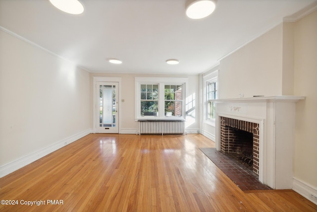 unfurnished living room featuring a fireplace, wood finished floors, baseboards, radiator heating unit, and crown molding