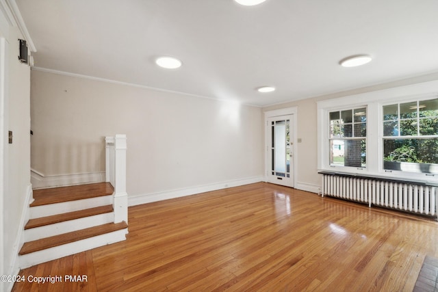 unfurnished room featuring light wood-type flooring, radiator heating unit, stairway, and ornamental molding