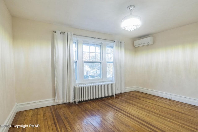 empty room with radiator heating unit, a wall unit AC, hardwood / wood-style flooring, and baseboards