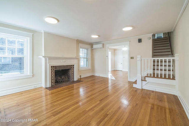 unfurnished living room with baseboards, a wall unit AC, stairway, wood finished floors, and a fireplace