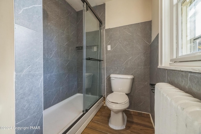 bathroom featuring tile walls, toilet, radiator heating unit, a shower stall, and wood finished floors