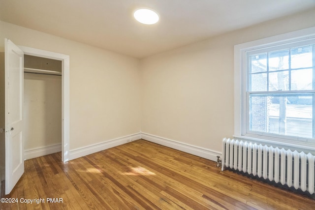 unfurnished bedroom with a closet, baseboards, radiator heating unit, and wood finished floors