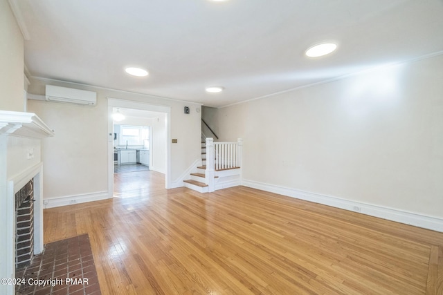 unfurnished living room featuring crown molding, a fireplace, a wall mounted AC, hardwood / wood-style floors, and stairs