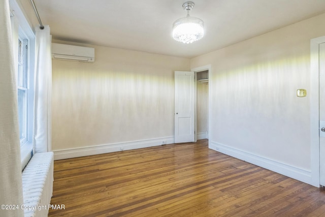 empty room featuring baseboards, hardwood / wood-style floors, and a wall mounted AC