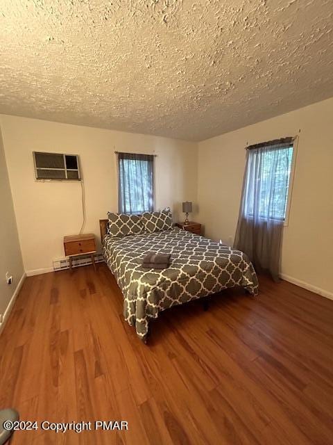 unfurnished bedroom featuring multiple windows, baseboards, a wall unit AC, and wood finished floors