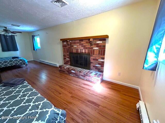 living room featuring a baseboard heating unit, a textured ceiling, visible vents, and wood finished floors