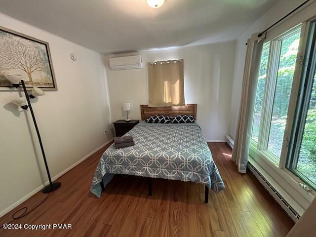 bedroom featuring a wall mounted AC, a baseboard heating unit, baseboards, and wood finished floors