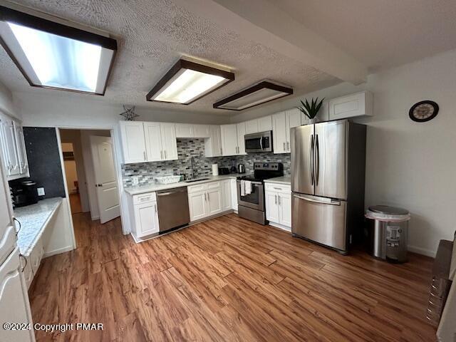 kitchen featuring white cabinets, tasteful backsplash, light wood-type flooring, and appliances with stainless steel finishes