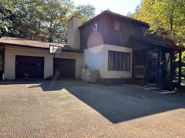 view of front of home featuring aphalt driveway, a garage, and a chimney