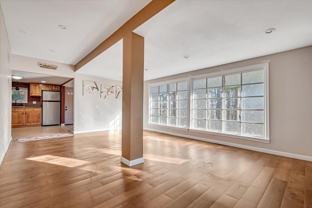 unfurnished living room featuring plenty of natural light, baseboards, and light wood-style floors