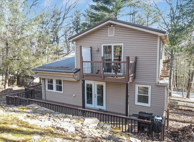 rear view of property featuring french doors, a balcony, metal roof, and a wooden deck