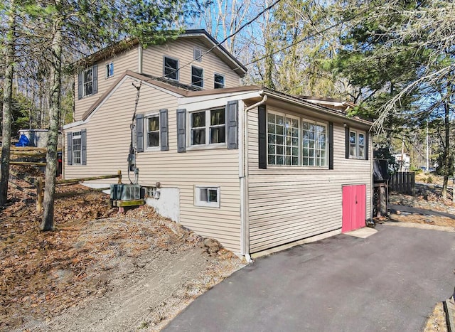 view of home's exterior with aphalt driveway, central AC, and fence