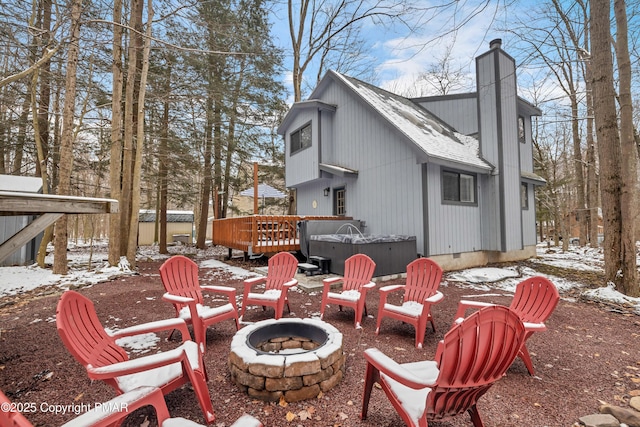 snow covered back of property with a deck, an outdoor fire pit, crawl space, a chimney, and a hot tub