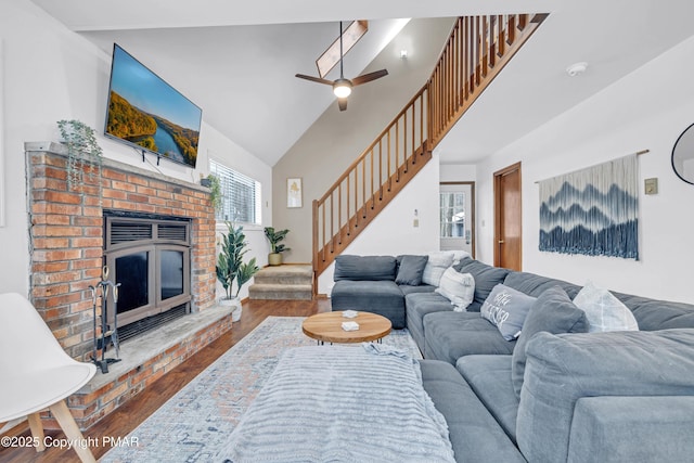 living room featuring stairway, a ceiling fan, wood finished floors, high vaulted ceiling, and a brick fireplace