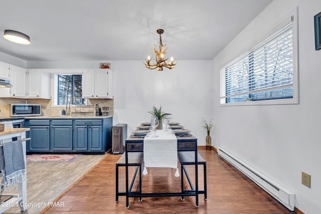 dining area featuring baseboards, wood finished floors, an inviting chandelier, and a baseboard radiator