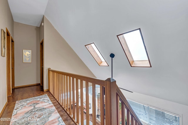 hall featuring baseboards, plenty of natural light, wood finished floors, and vaulted ceiling with skylight