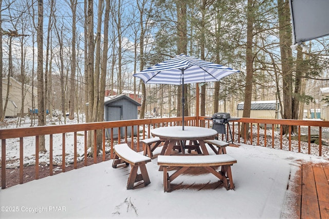 snow covered deck with outdoor dining area, a storage unit, and an outbuilding