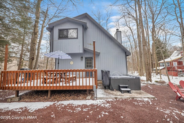 snow covered back of property featuring a deck, a chimney, and a hot tub