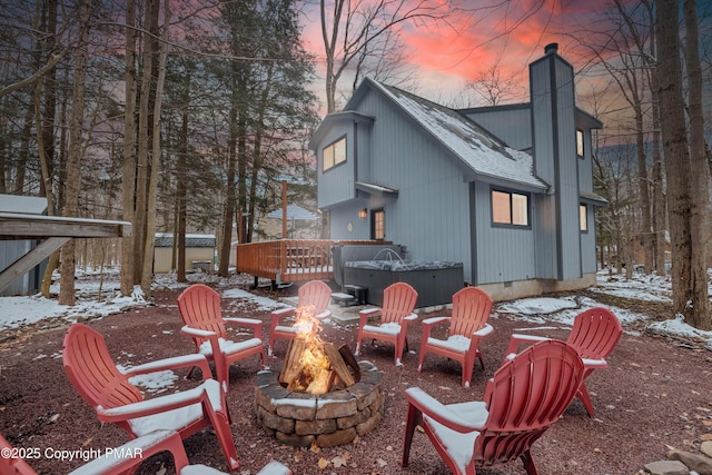 snow covered rear of property featuring roof with shingles, a hot tub, a chimney, a fire pit, and crawl space