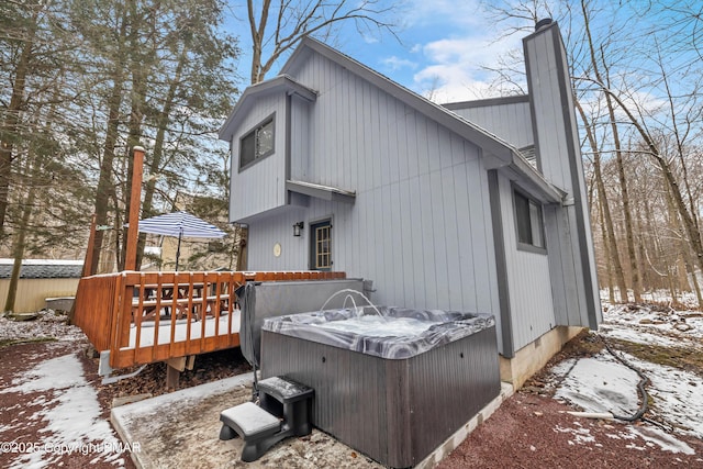 view of snowy exterior featuring a deck, a chimney, and a hot tub