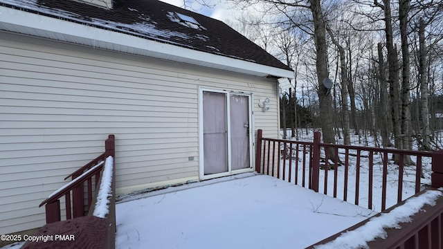 snow covered property entrance featuring a shingled roof