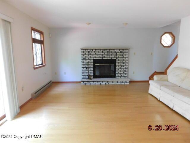 unfurnished living room with stairway, baseboards, a baseboard radiator, light wood-style flooring, and a brick fireplace